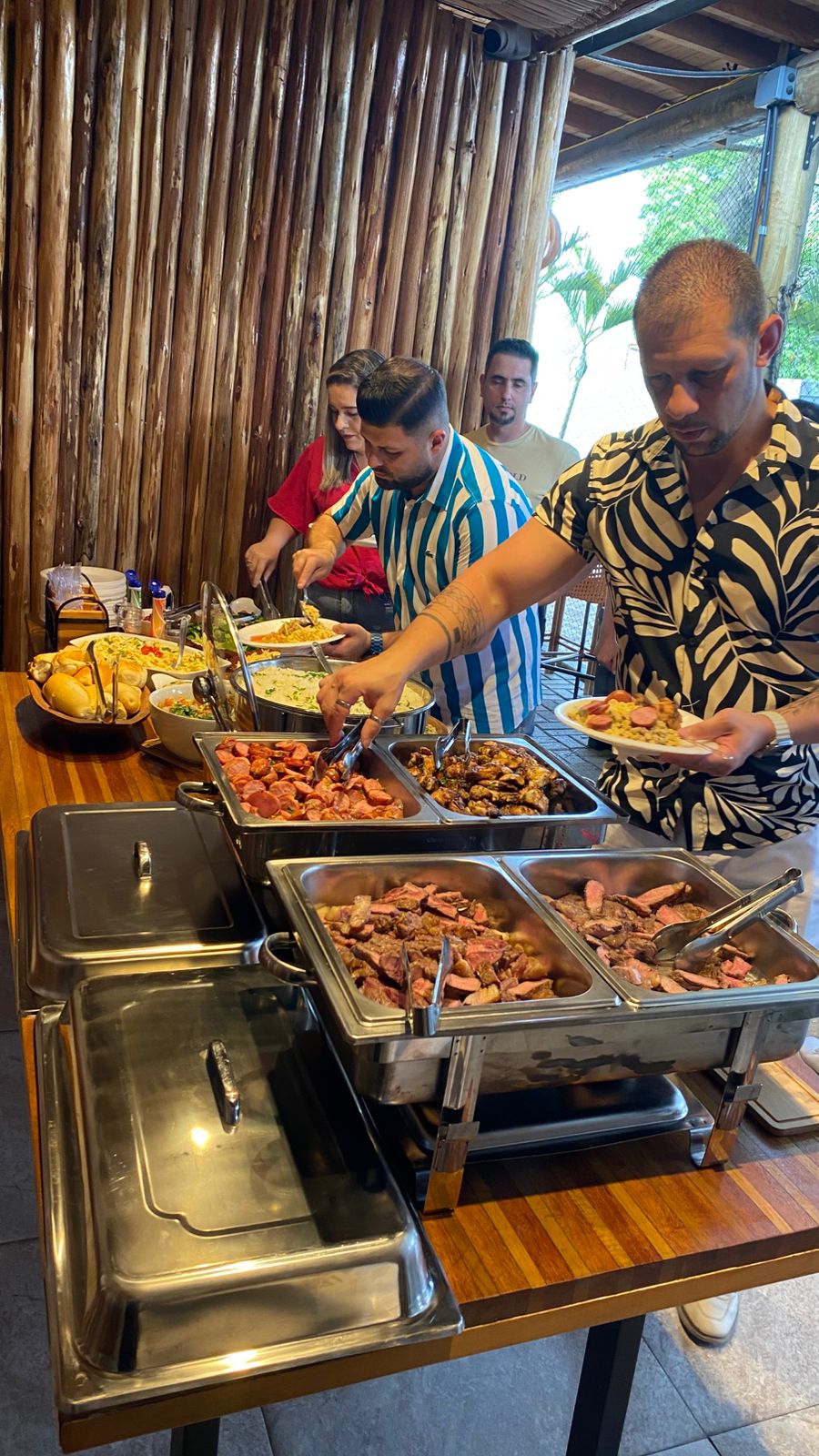 Convidados se servindo de carnes e acompanhamentos em um buffet